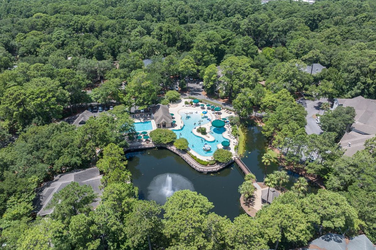 Vista aérea de un resort con una zona de piscina central rodeada de exuberante vegetación y una masa de agua.