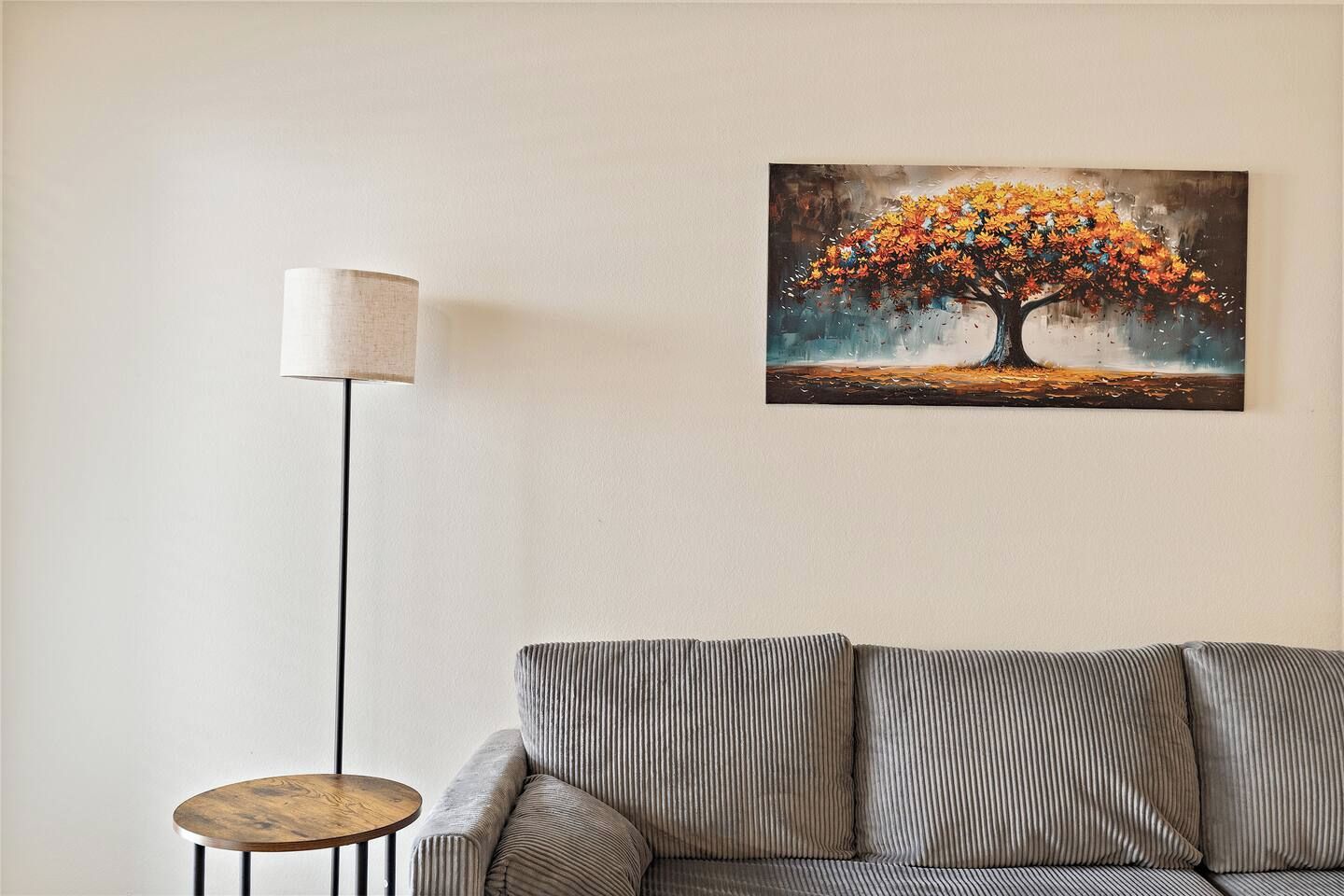 A living room with a sofa, a floor lamp, and a painting of a tree.