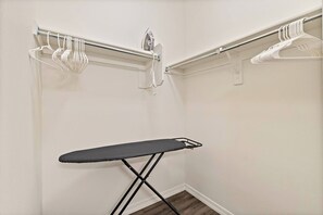 Une petite pièce équipée d’un espace dédié au repassage, d’un portant et d’un fer à repasser fixé au mur.