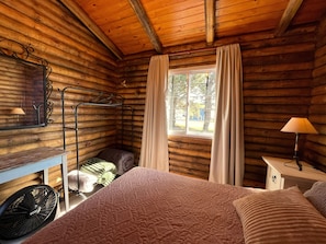 A log cabin room with a bed, a desk, a chair, a window with curtains, and a fan. - New Listing (Ostende)