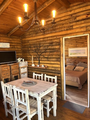 Ein rustikaler Holzraum mit Essbereich, Fernseher und einem Schlafbereich mit Bett und Kissen.