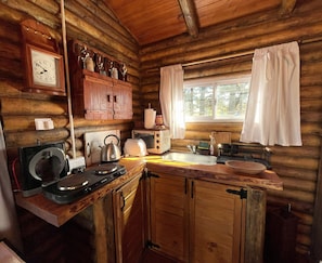 A rustic cabin interior with a wooden interior, a clock, a kettle, a toaster, and a window with curtains. - New Listing (Ostende)
