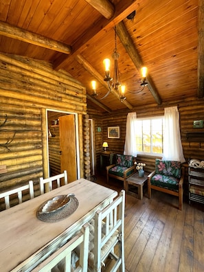A rustic wooden cabin interior with a dining table, chairs, a sofa, and a chandelier. - New Listing (Ostende)