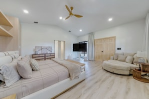 Un salon spacieux avec un grand lit, un canapé, une télévision et un ventilateur de plafond.
