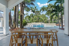 Un espace extérieur abrité, doté d’une piscine, entouré de palmiers et comprenant une table à manger avec des chaises.