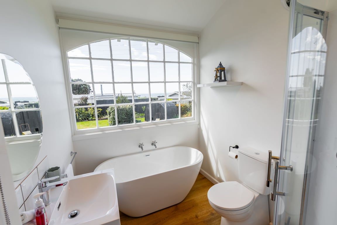 Een badkamer met een vrijstaand bad, een toilet, een wastafel en een raam met uitzicht op de omgeving.
