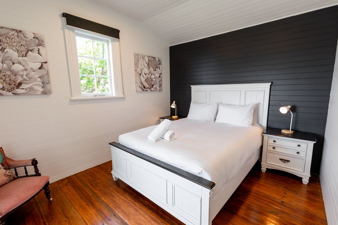 Una camera da letto con un letto bianco, pavimento in legno, un comodino con una lampada e opere d'arte alle pareti.