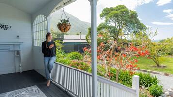 Un portico coperto con ringhiera bianca, un vaso pensile e vista su un giardino con diverse piante e alberi.