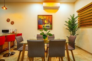 A dining area with a glass table, four chairs, a potted plant, and a painting on the wall. - Elegant 2BR Condo with Pool in Vibrant La Paz (lA paZ)
