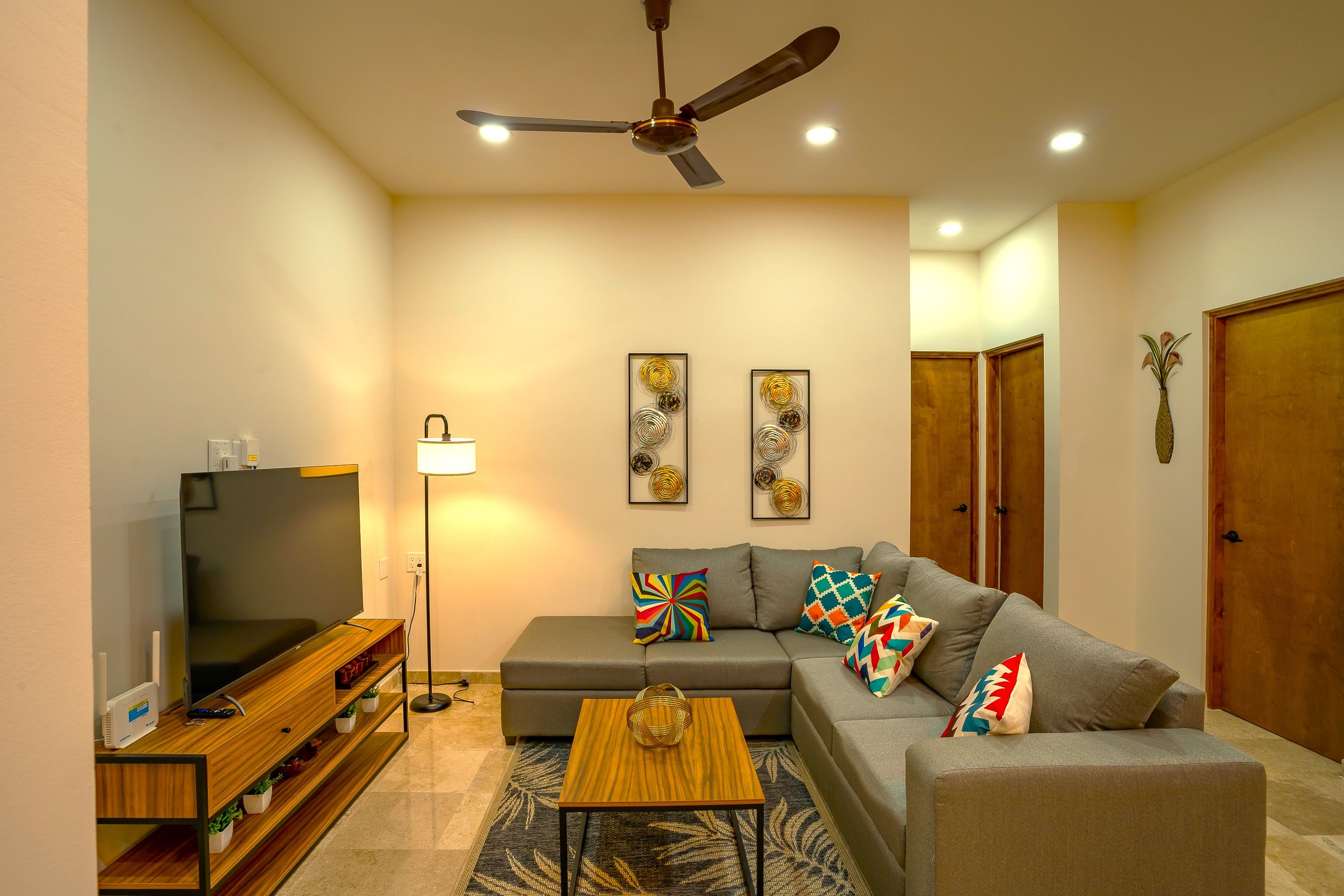 A modern living room with a flat-screen TV, a ceiling fan, a sofa, a coffee table, and decorative wall art.