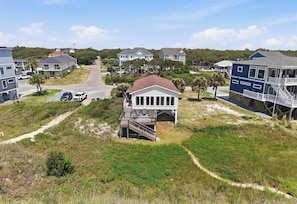 A coastal residential area with houses, a prominent white house with a porch, and a blue house with a balcony. - Oceanfront Bliss! Panoramic Views! Newly Renovated! Yaupon Beach, Oak Island, NC (Oak Island)