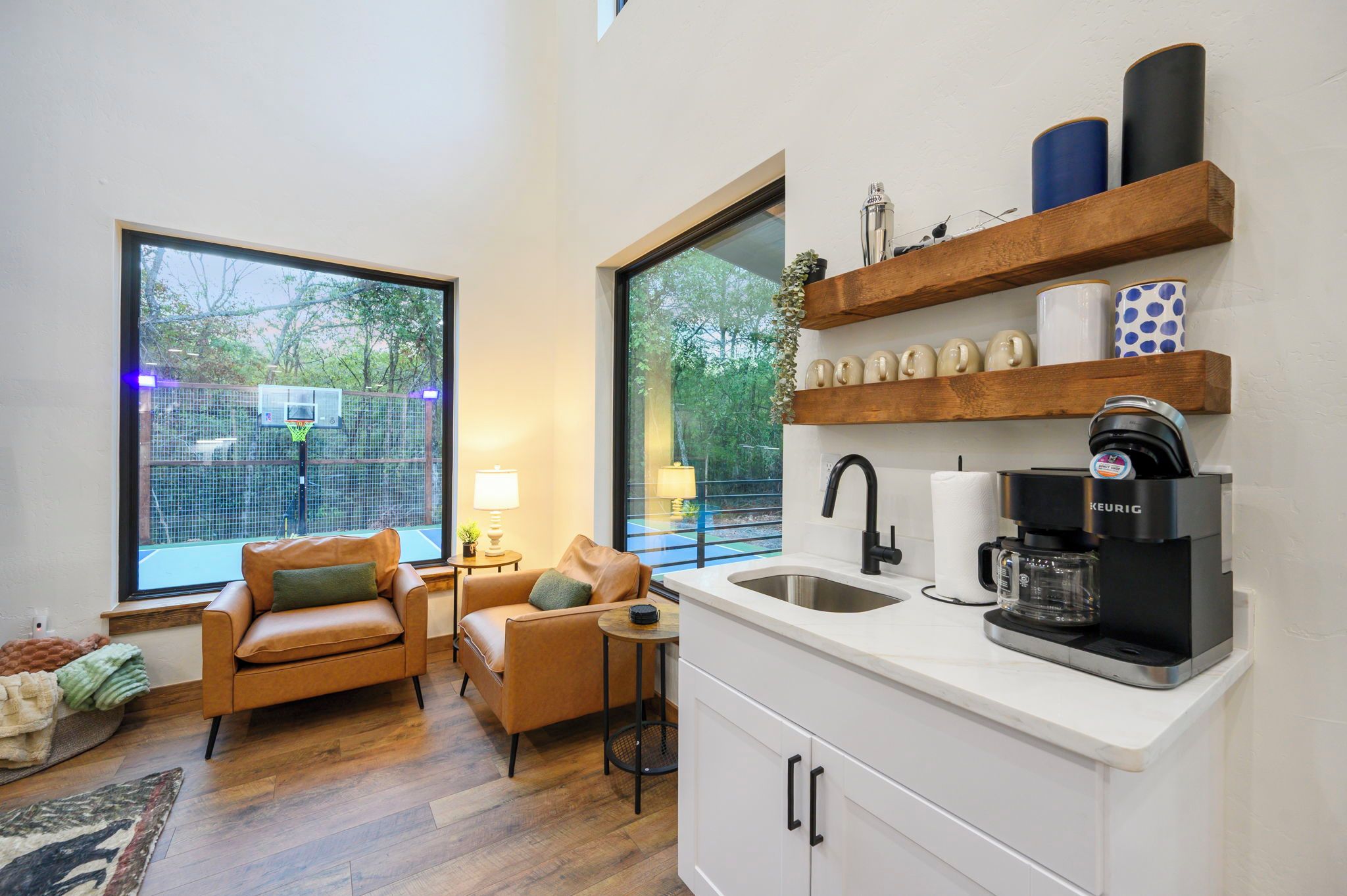 Een moderne keuken met een koffiezetapparaat, een spoelbak en een raam met uitzicht op een basketbalveld.