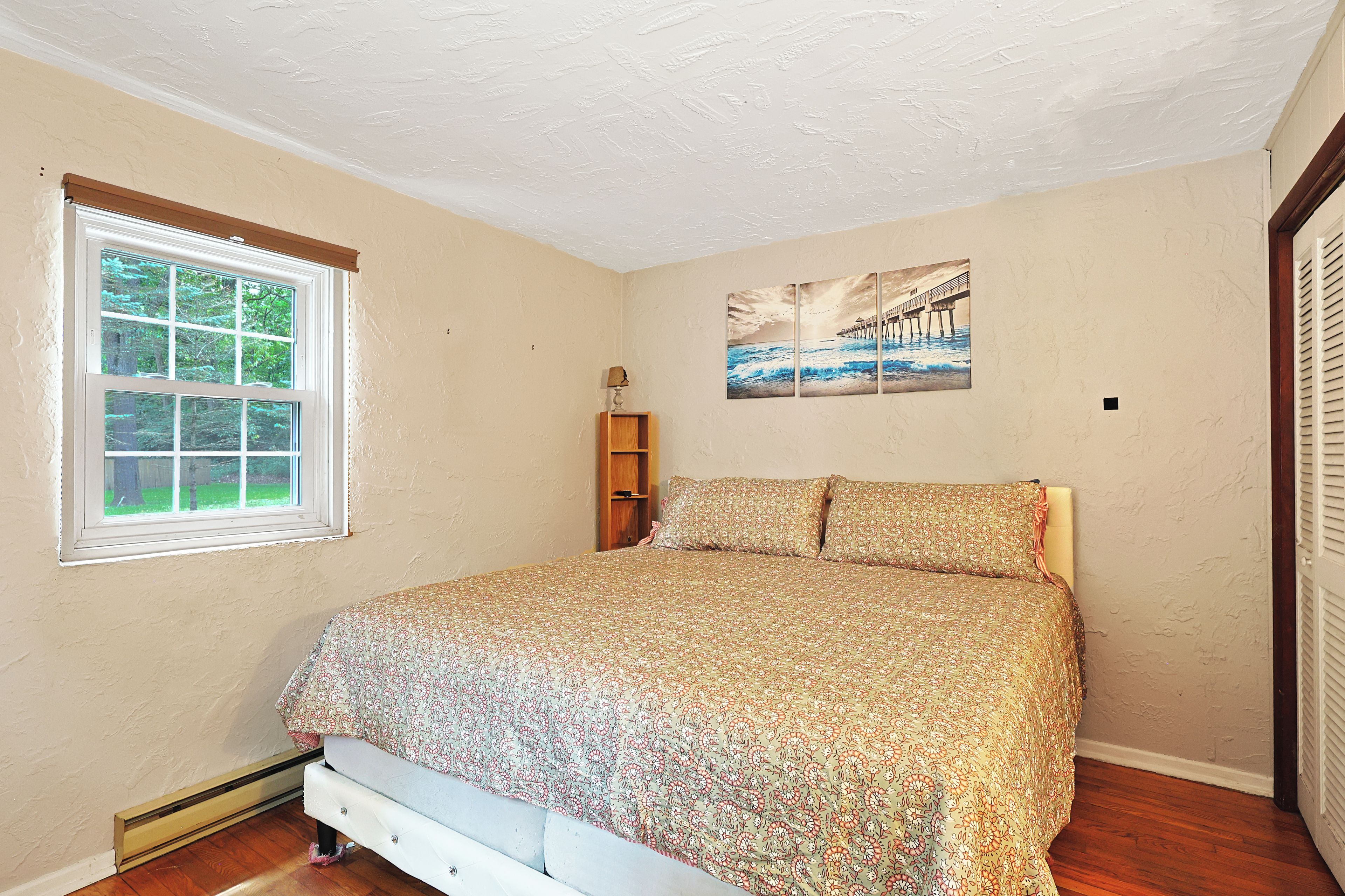 Une chambre à coucher avec un lit, une fenêtre, une étagère fixée au mur et un tableau.