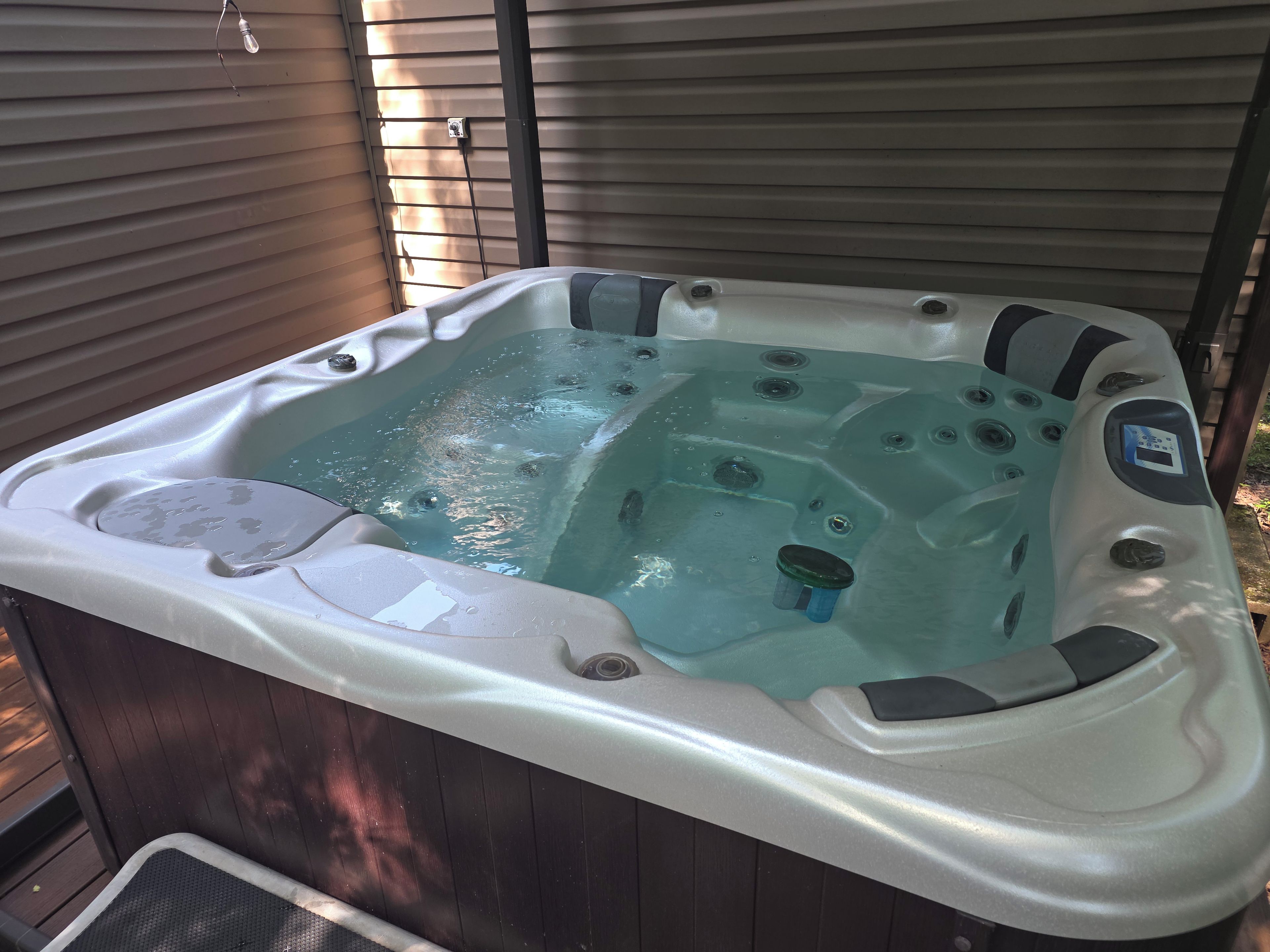 A hot tub with a control panel, built-in jets, and a footrest.