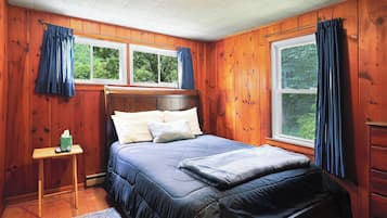 A wooden-paneled bedroom with a bed, two windows, a nightstand, and a dresser.