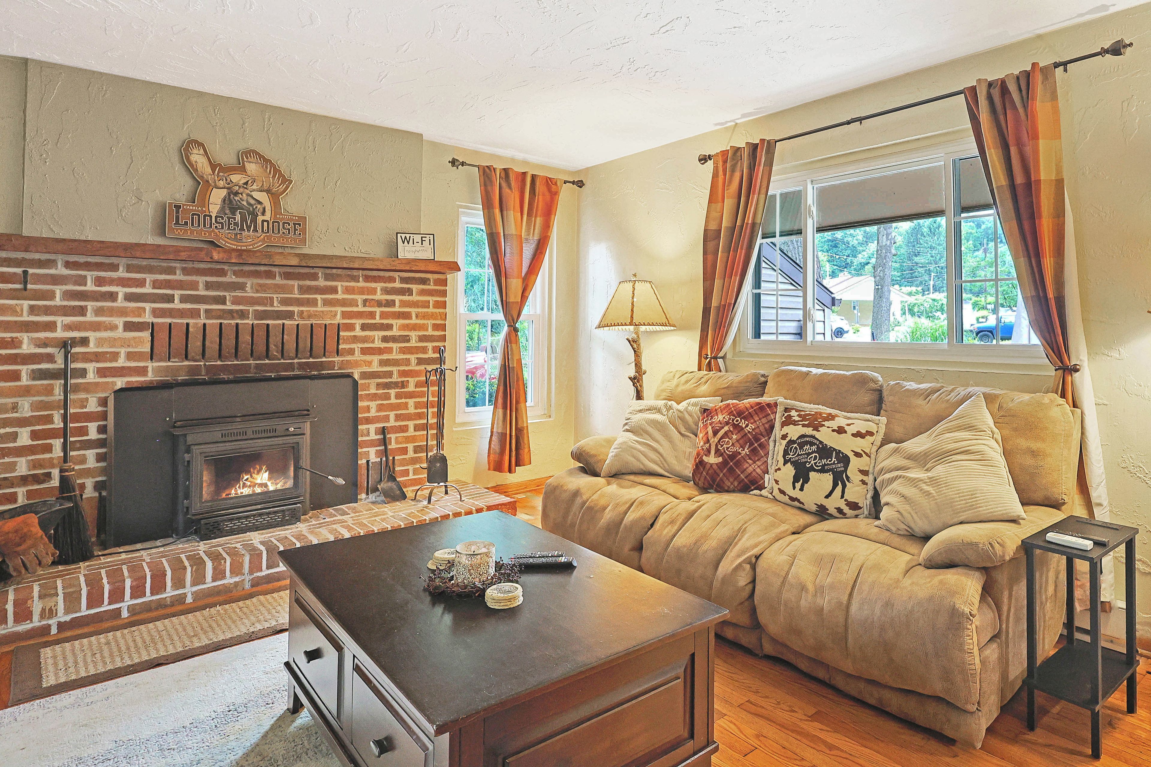 A cozy living room with a fireplace, a sofa with decorative pillows, a coffee table, and a window with curtains.