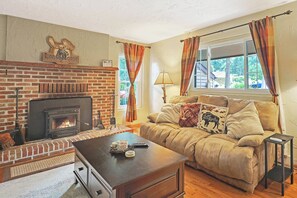 Ein gemütliches Wohnzimmer mit Kamin, einer Couch mit dekorativen Kissen, einem Couchtisch und einem Fenster mit Vorhängen.