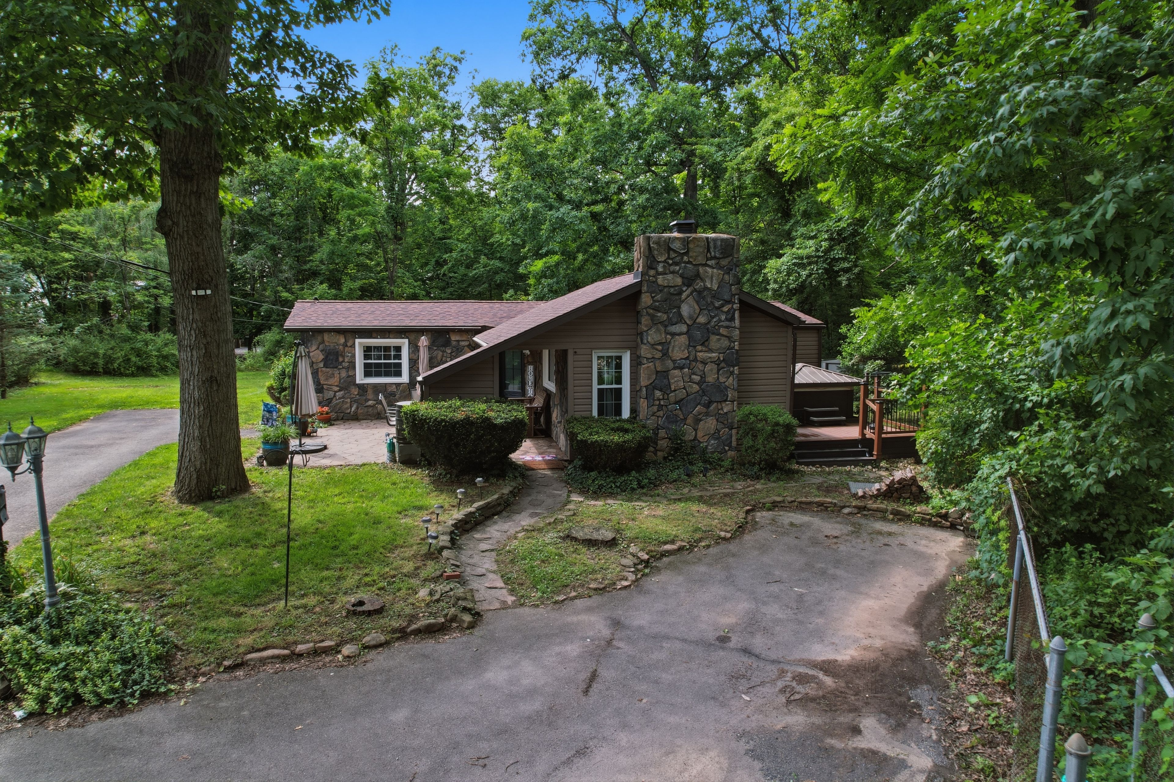 A stone house with a chimney, surrounded by lush greenery and a paved driveway.
