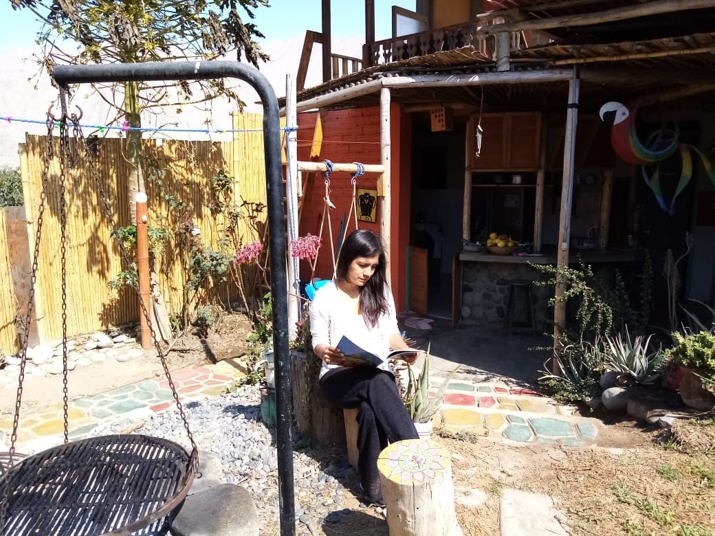A person sitting on a swing chair in a garden area with a wooden fence and a house in the background.