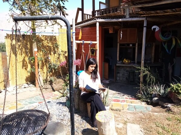 A person sitting on a swing chair in a garden area with a wooden fence and a house in the background.