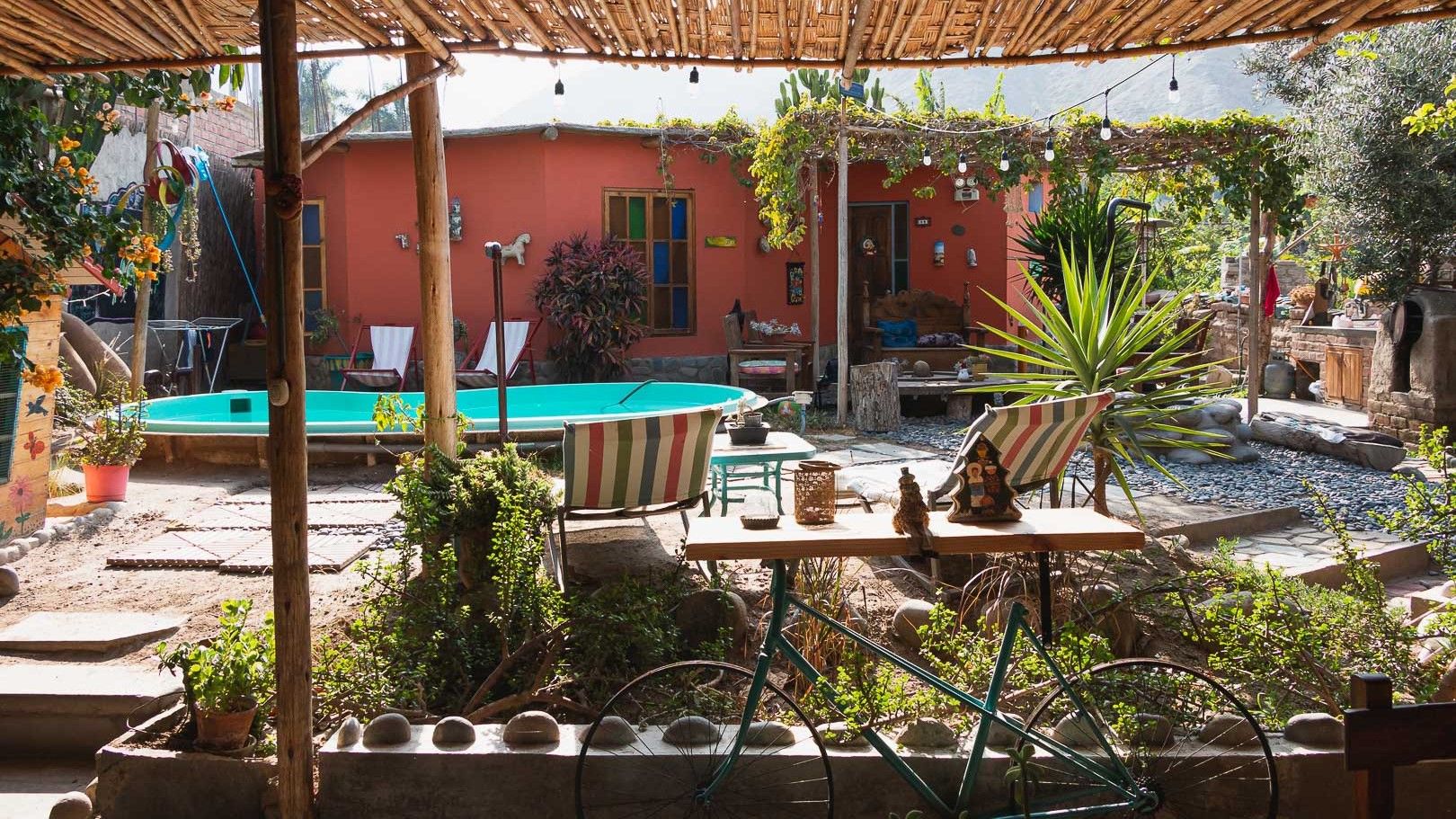 A pool area with a table and chairs, surrounded by plants and a wooden pergola.