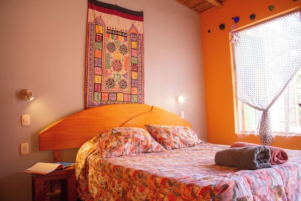 A bedroom with a wooden headboard, a floral bedspread, and a wall hanging.