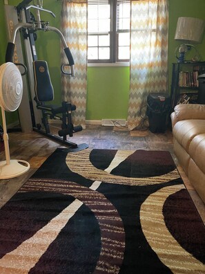 Ein Zimmer mit Fitnessgerät, Ventilator, einer Couch und einem gemusterten Teppich.
