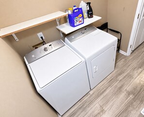 A laundry area with a front-loading washer and dryer, a shelf with cleaning supplies, and a power outlet. - 3 King Beds • Fenced Yard • Pet-Friendly • Guest Favorit • Great location (Pooler)