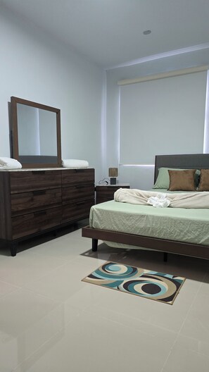 Une chambre à coucher avec un lit, une commode, un miroir, une table de chevet et une fenêtre.