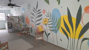A room with a ceiling fan, two wicker chairs, a patterned rug, and a wall with a floral mural. - New boutique-apartments complex with AC WIFI, amenities in San Juan close to all (San Juan)