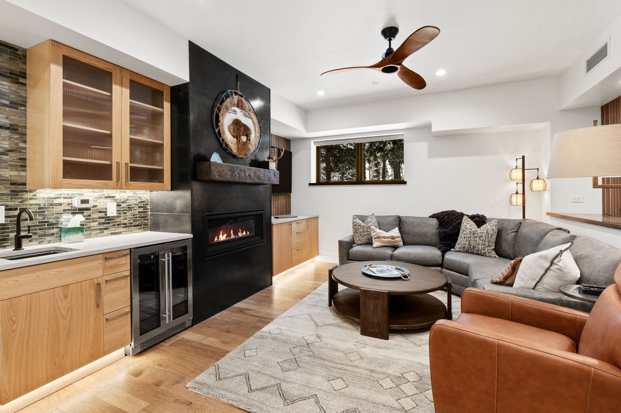 Una cocina moderna con horno empotrado y chimenea, un conjunto de sofá gris y un ventilador de techo.