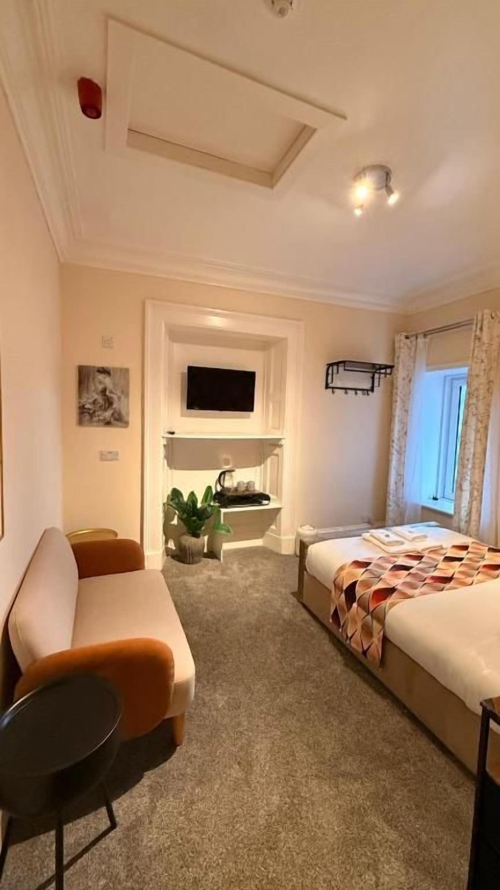 A hotel room with a bed, a sofa, a small table, a TV mounted on the wall, and a window with curtains.
