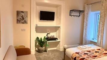 A hotel room with a bed, a sofa, a small table, a TV mounted on the wall, and a window with curtains.