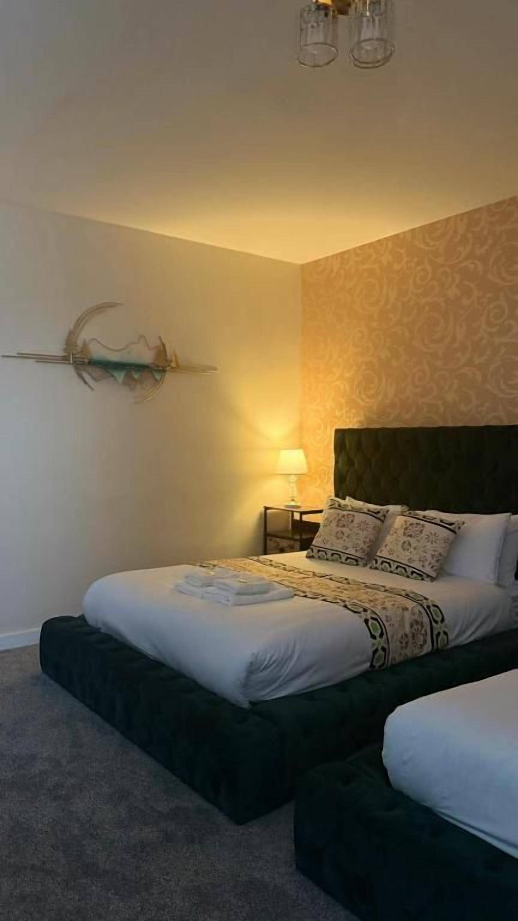 A bedroom with two beds, a nightstand, a lamp, and a wall-mounted decor piece.