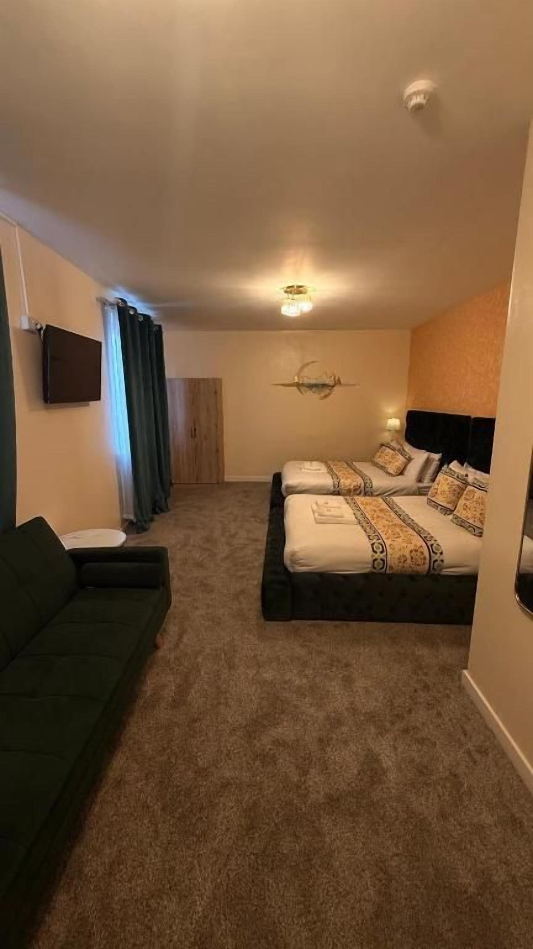 A hotel room with two beds, a sofa, a flat-screen TV, and a ceiling light.