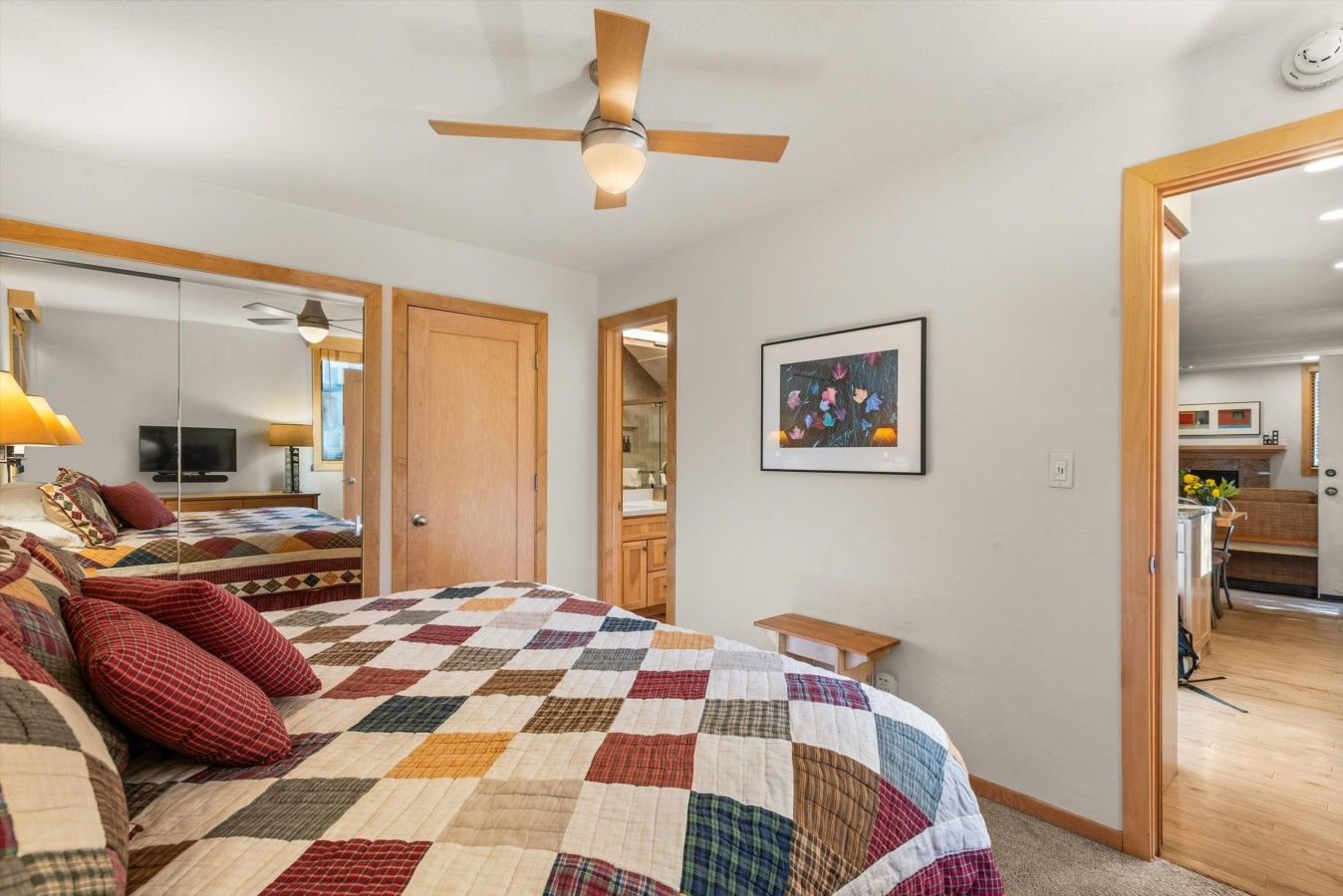 A bedroom with a large bed, a ceiling fan, a mirror, and a painting on the wall.