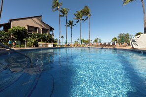 Ein klares Schwimmbecken mit Liegestühlen und Palmen, umgeben von einem Gebäude mit einem Balkon.