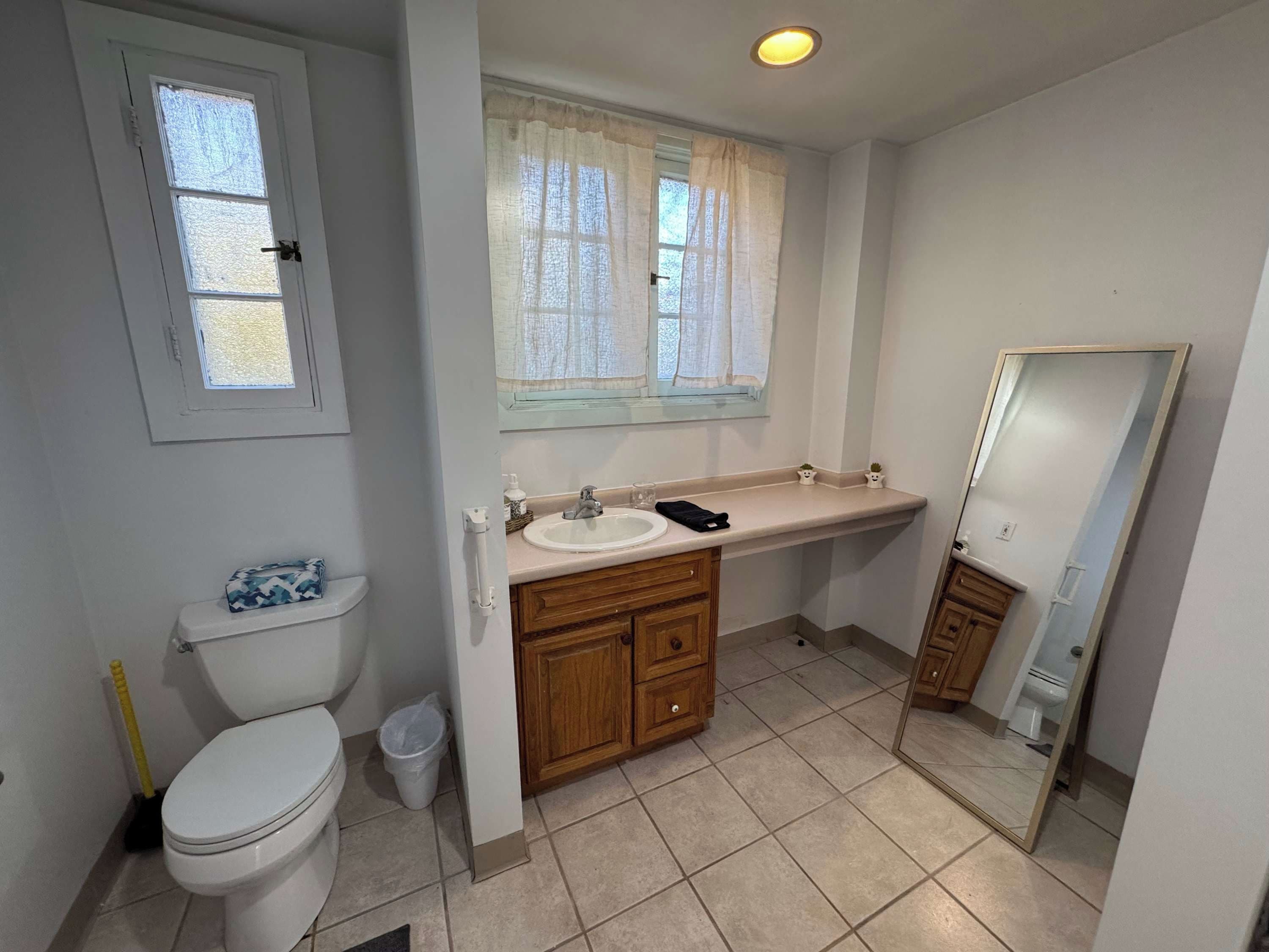 Une salle de bain avec des toilettes, un lavabo, un miroir et une fenêtre.