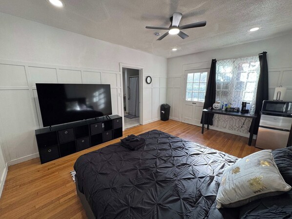 Ein Schlafzimmer mit einem Bett, einem Fernseher, einem Deckenventilator, einem Fenster und einer Küchenzeile.
