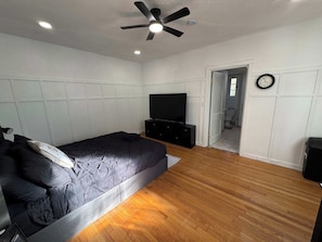 Ein Schlafzimmer mit einem Bett, einem Fernseher, einem Deckenventilator und einer Tür zu einem Badezimmer.