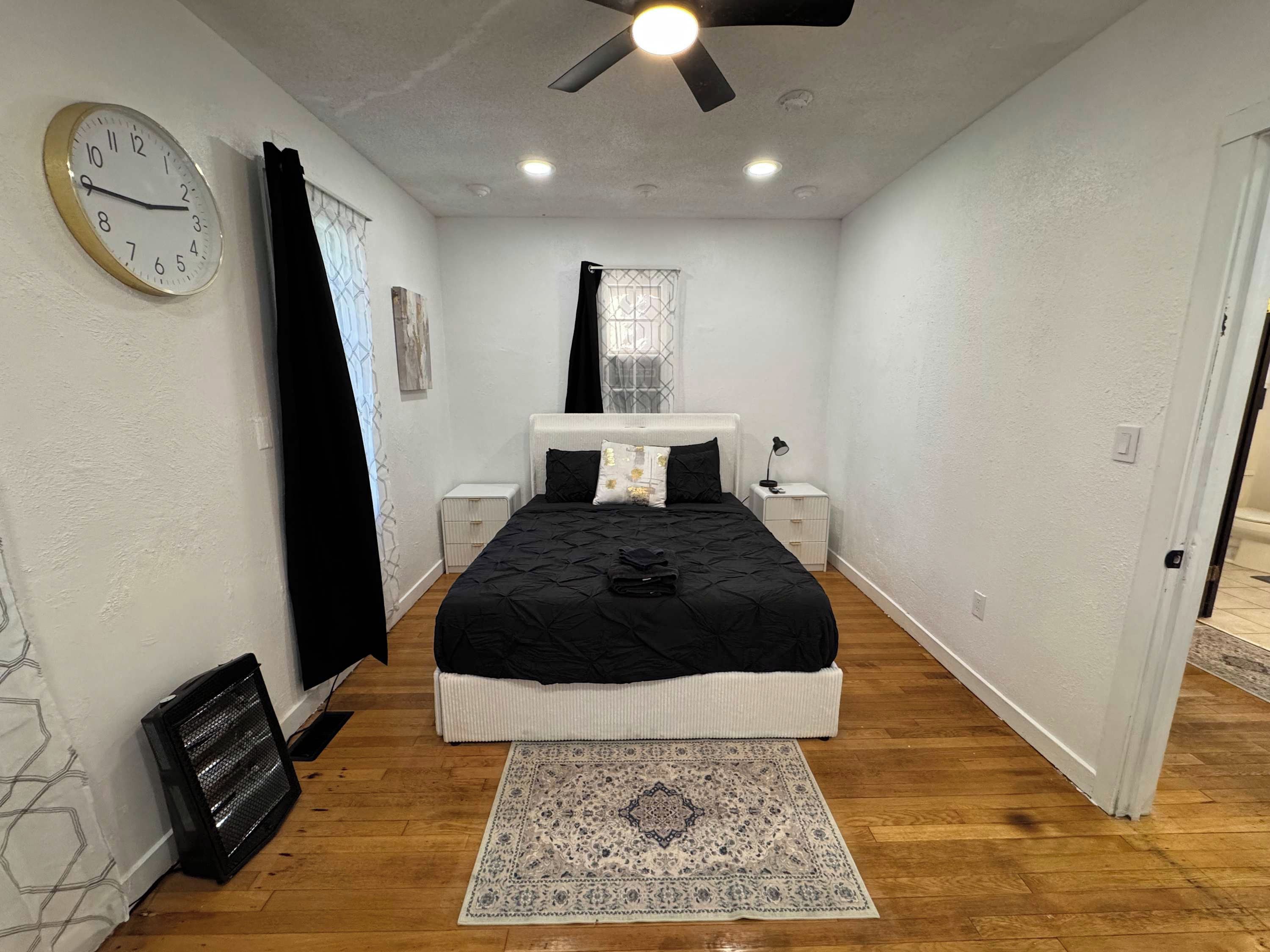 Una camera da letto con un letto, comodini, una sveglia, una ventola a soffitto e un tappeto.