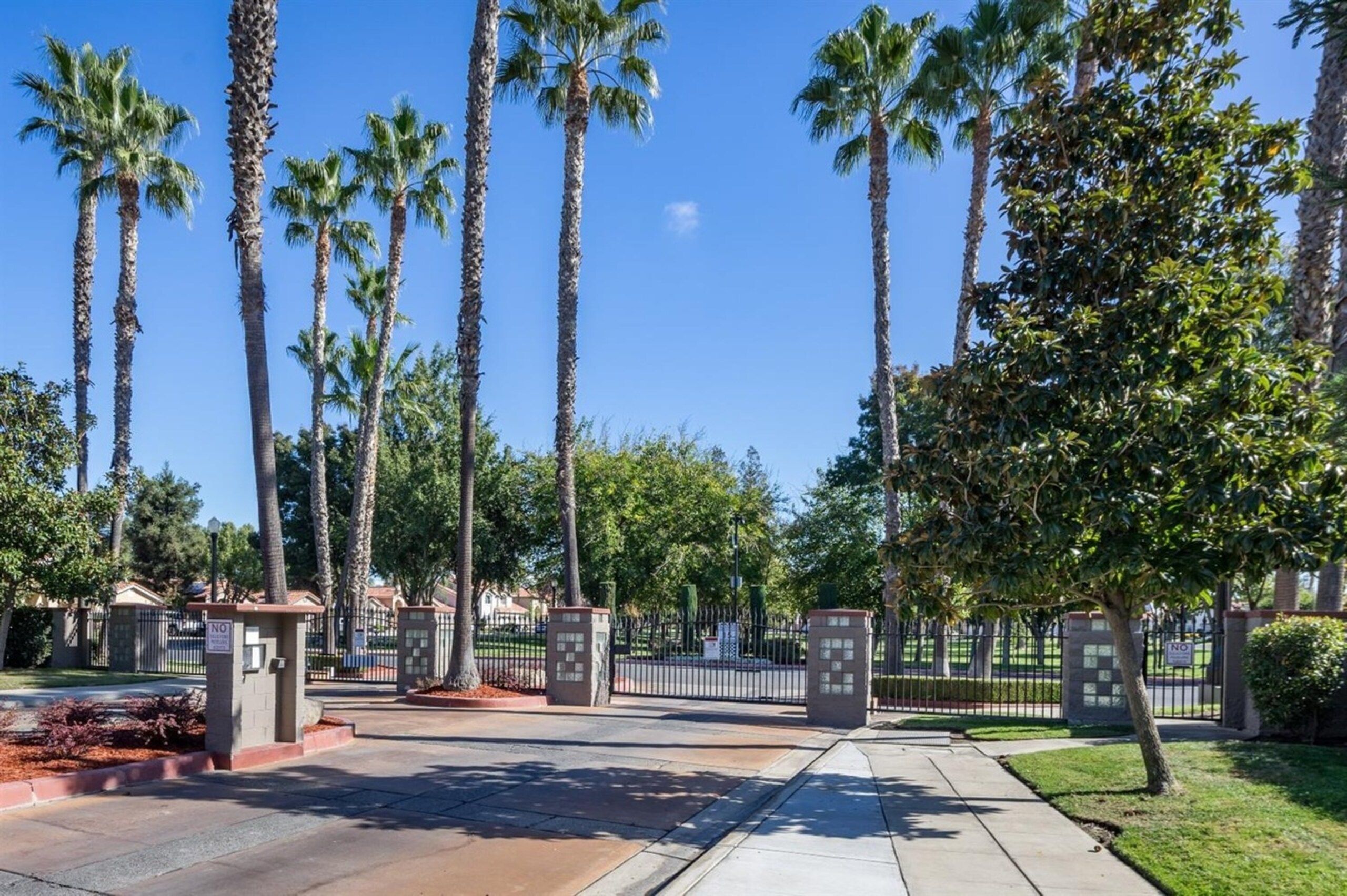 A gated entrance with palm trees and a clear sky.