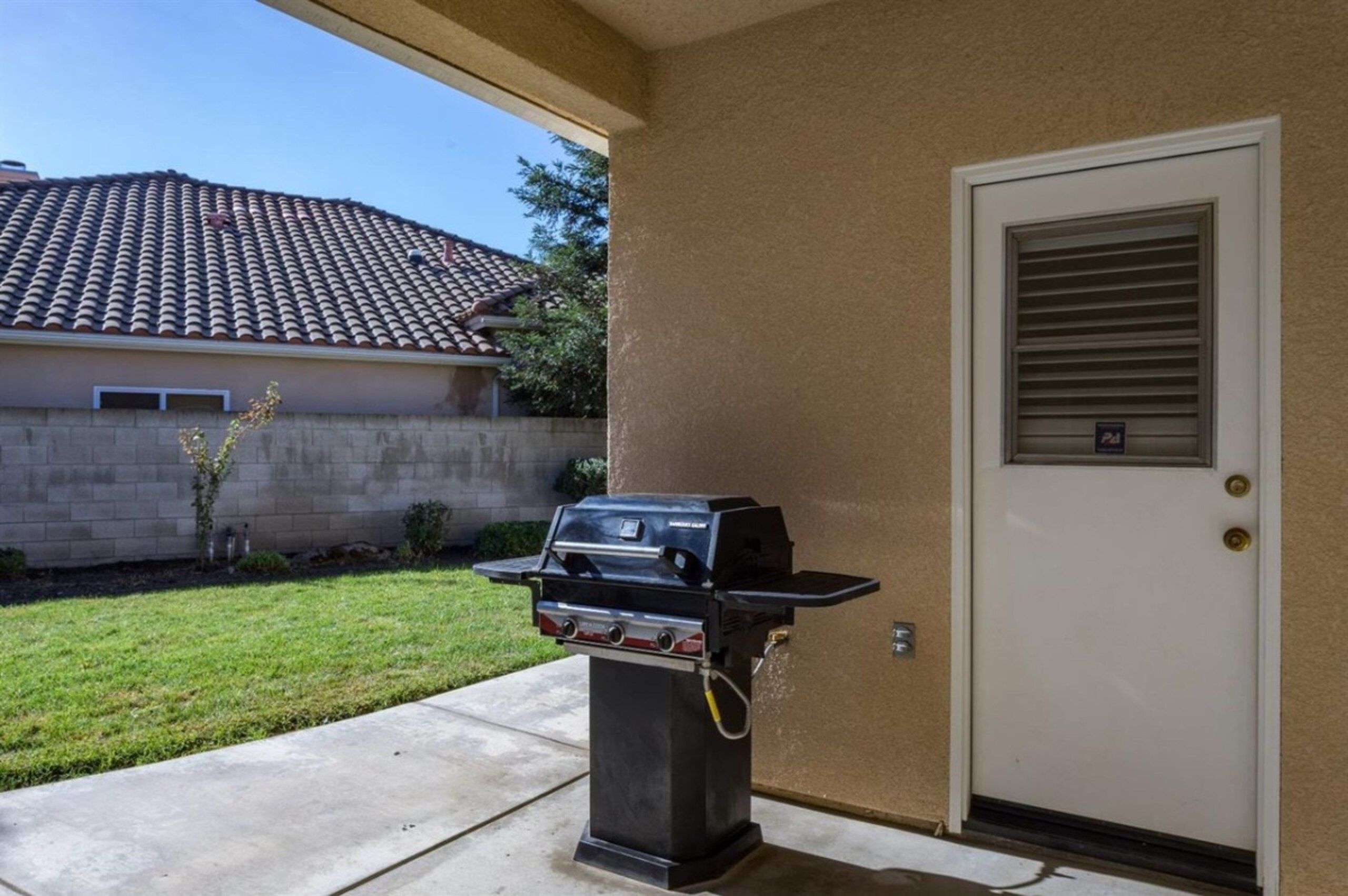 A barbecue grill outside a house with a tiled roof and a door with a window.