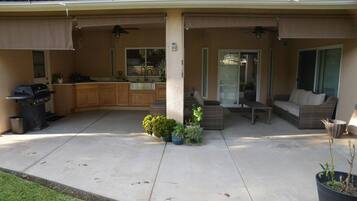 A covered patio with a kitchen area, outdoor seating, and a grill.