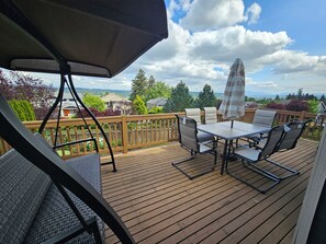 Eine Holzterrasse mit Tisch, Stühlen und einer Hängesitzgelegenheit, mit Blick auf ein Wohngebiet.