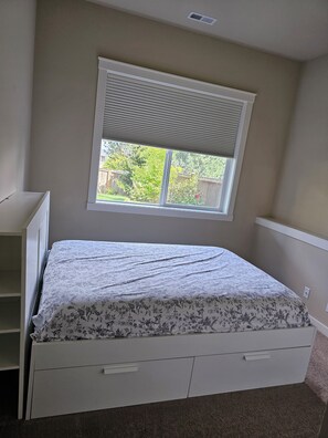 Ein Schlafzimmer mit einem Bett, einem Fenster mit Jalousien, einer weißen Kommode und einem Teppichboden.