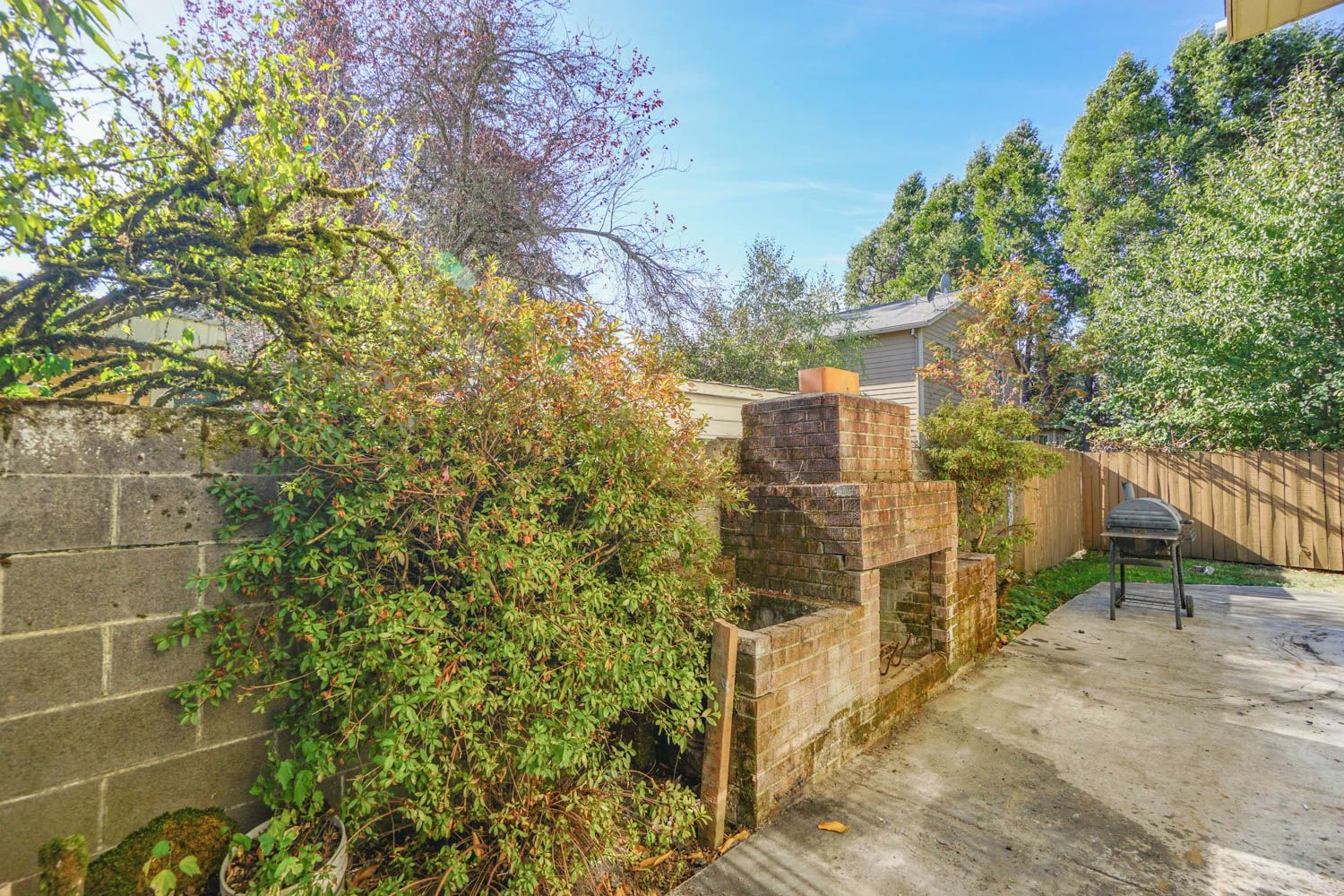 A backyard with a brick barbecue area, a wooden fence, and a concrete patio.