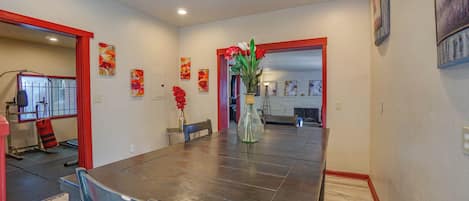 Un comedor con una mesa de madera oscura, sillas, un florero con flores y un marco rojo en un acceso a la cocina.
