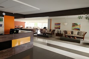 A modern lobby with a reception desk, seating area, and artwork on the walls. - Apto 3 Suítes p/ 10 pessoas e lazer (Rio Quente)