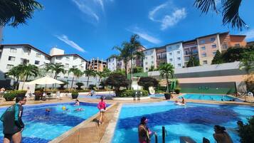 Un área de piscina con varias piscinas, palmeras y un edificio de varios pisos al fondo.